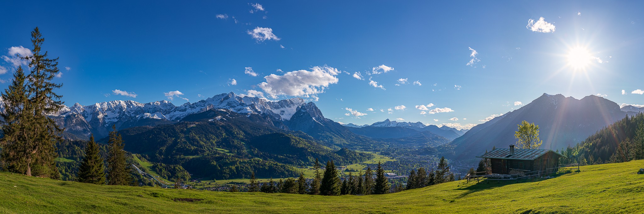 Garmisch-Partenkirchen mit Zugspitze und Almhütte Eckenhütte. Idyllisches Bergpanorama in den bayerischen Alpen auf Garmisch-Partenkirchen und die Zugspitze mit Eckenhütte.