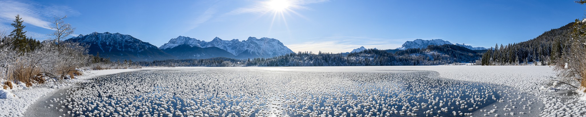 Eisrosen - Panorama am Barmsee. Winterlandschaft am zugefrorenen See. Eiskristalle auf dem Spiegeleis mit Blick ins Bergpanorama.