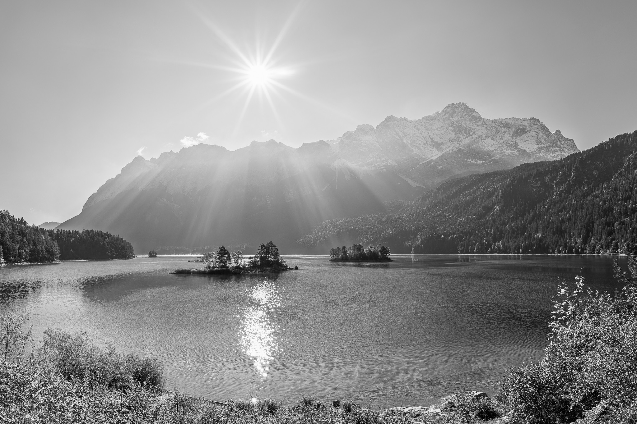 Eibseeblick mit Zugspitze sw. Naturparadies am Eibsee. Inseln im türkisen Wasser und die Sonne strahlt über dem Zugspitzmassiv.
