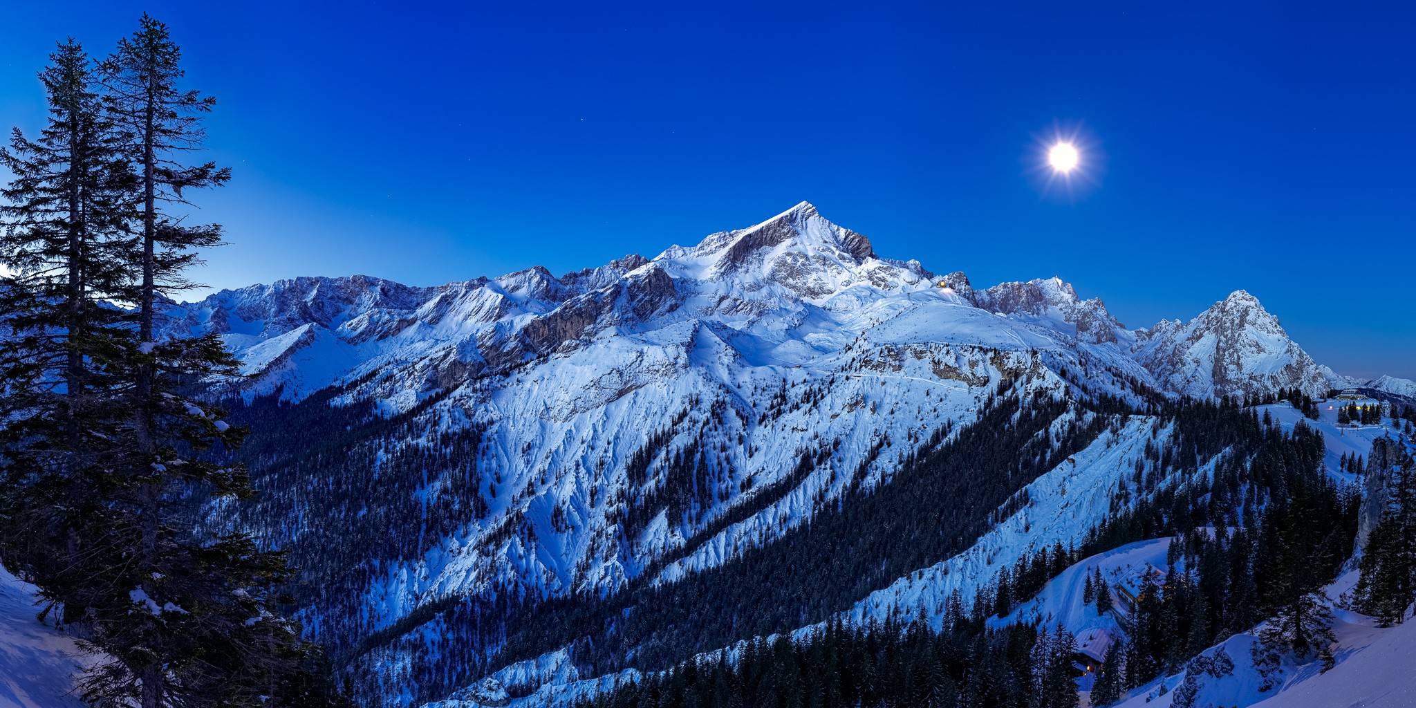 Garmisch-Partenkirchen - Winter. Blick auf die Alpspitze und die Zugspitze vom Kreuzjoch bei Mondlicht. Auf der linken Seite sehen sie den Stuiben, weiter rechts die Hochalm und auf der rechten Seite das Kreuzeckhaus. Unten rechts ist die Barbarahütte.